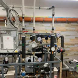 Kompleksowa instalacja hydrauliczna z rurami, zaworami, manometrami i tablicą sterowniczą. Widoczne detale montażu i podłączenia. Profesjonalny układ instalacji w pomieszczeniu technicznym.