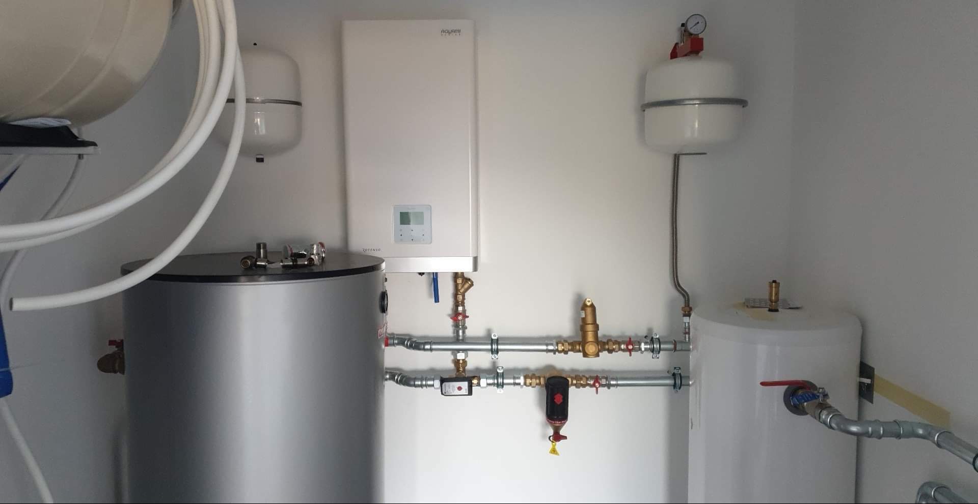 Kompletna instalacja grzewcza z zbiornikami, rurami i kotłem Aquami, zamontowana w pomieszczeniu technicznym, prezentująca precyzję wykonania i nowoczesne rozwiązania.