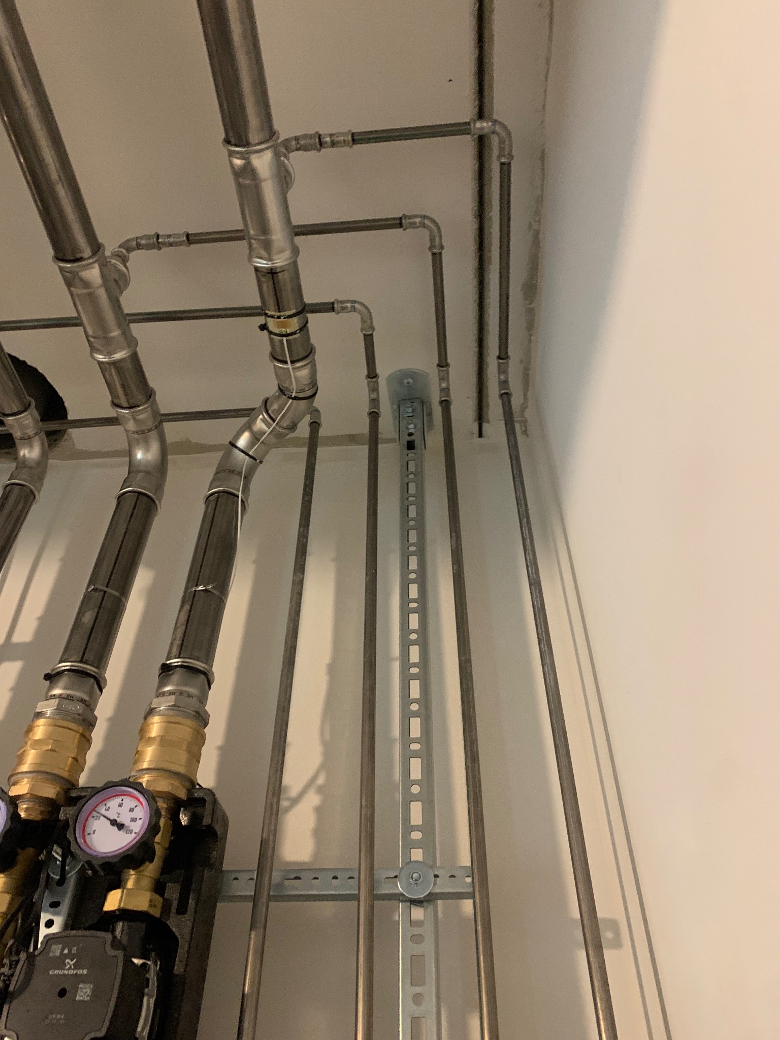 Nowoczesna instalacja grzewcza z rurami ze stali nierdzewnej, manometry na pompie obiegowej, montaż na szynach. Widok z dołu.