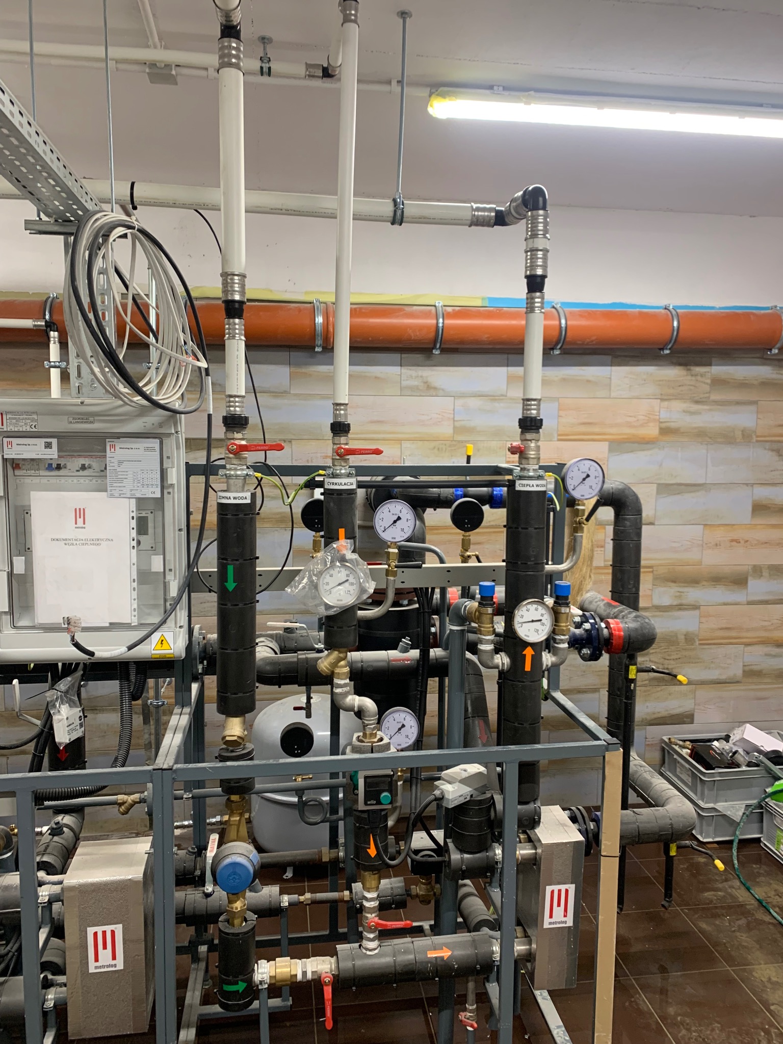 Kompleksowa instalacja hydrauliczna z rurami, zaworami, manometrami i tablicą sterowniczą. Widoczne detale montażu i podłączenia. Profesjonalny układ instalacji w pomieszczeniu technicznym.