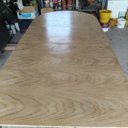 Renesans drewna - Odnowiony, rozkładany blat drewnianego stołu z widocznym rysunkiem słojów, po renowacji. Jasne drewno, gładka powierzchnia. W tle widoczne narzędzia i pojemniki.