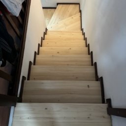 Renesans drewna - Jasne drewniane schody z ciemnymi obramowaniami widziane z góry, prowadzące w górę, z fragmentem błękitnej skarpetki w dolnej części kadru.