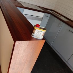 Renesans drewna - Lakierowany blat drewniany w kuchni, z widoczną puszką oleju do drewna Osmo. Ujęcie z niskiego kąta, podkreślające strukturę drewna i wykończenie blatu.