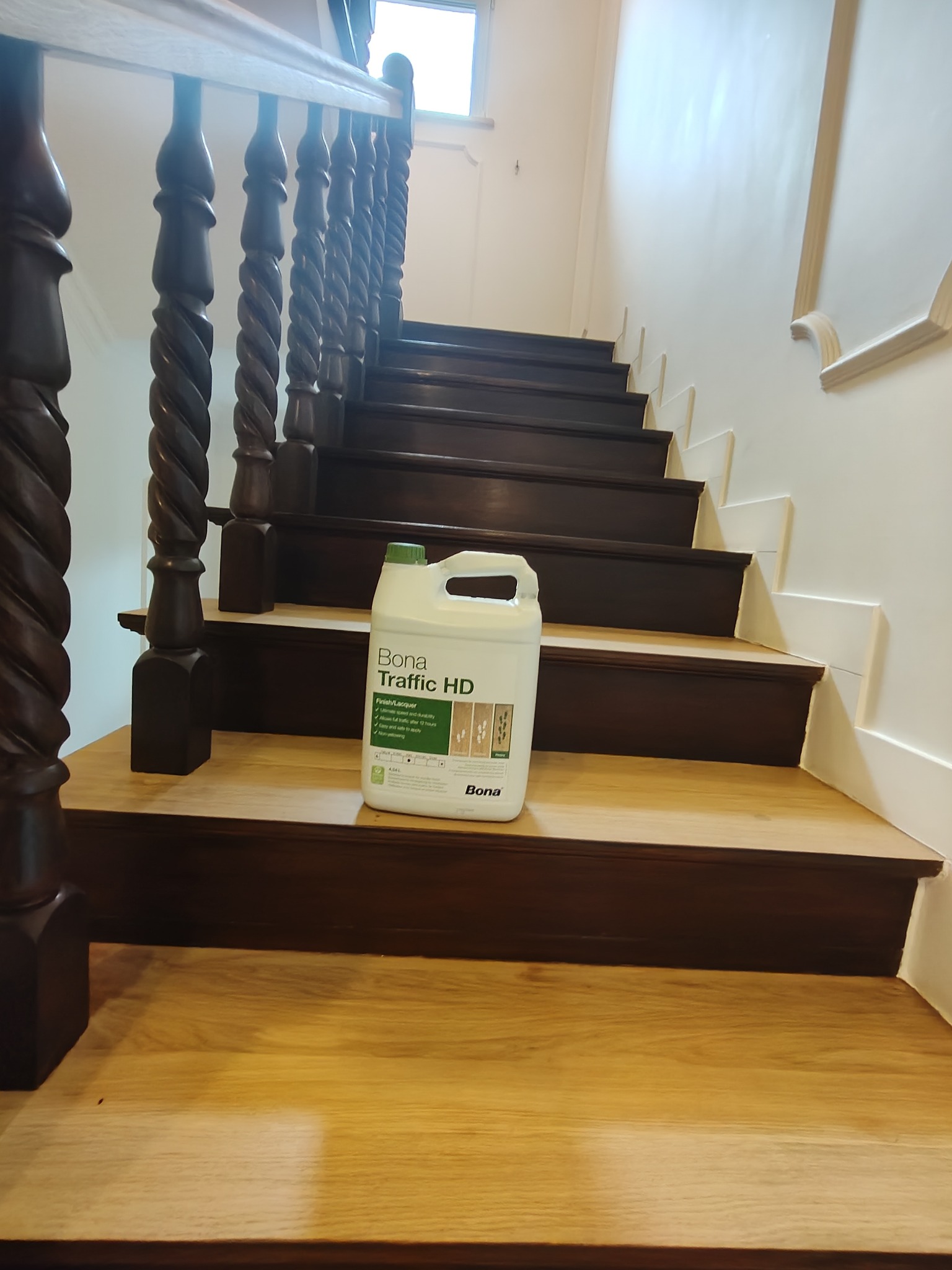 Lakier Bona Traffic HD na drewnianych schodach z ozdobną balustradą. Widok z dołu na jasne stopnie i ciemniejsze podstopnice. Wykończenie po renowacji.