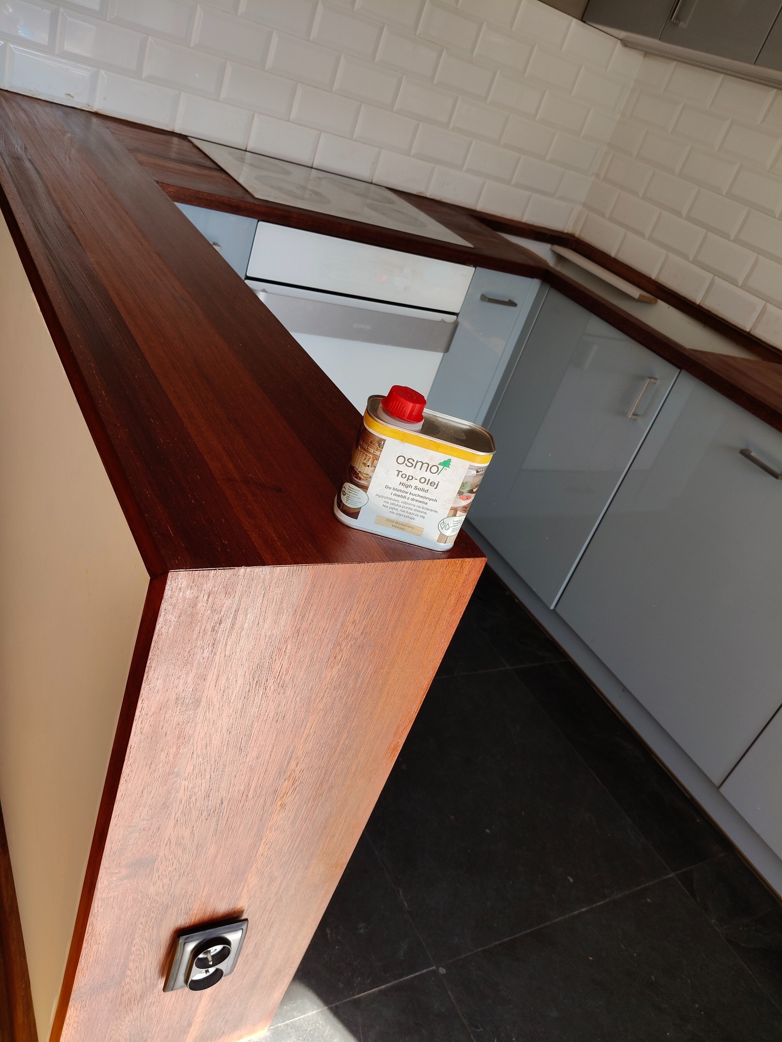 Lakierowany blat drewniany w kuchni, z widoczną puszką oleju do drewna Osmo. Ujęcie z niskiego kąta, podkreślające strukturę drewna i wykończenie blatu.
