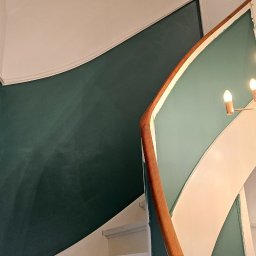 MADO Mateusz Dowejko - Klatka schodowa po malowaniu: ściany w odcieniach zieleni i bieli, drewniana balustrada. Widok z dołu, schody pomalowane na biało. Estetyczne wykończenie.