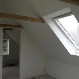 MADO Mateusz Dowejko - Poddasze po remoncie: białe ściany, drewniane belki stropowe, okno dachowe. Widok na sąsiedni pokój z oknem. Minimalistyczny styl, świeżo po malowaniu.