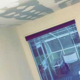 MADO Mateusz Dowejko - Szpachlowany sufit z widocznymi łatami gładzi, przygotowany do malowania. W tle okno z widokiem na ogród zimowy.