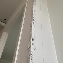 MADO Mateusz Dowejko - Zamontowany narożnik aluminiowy z perforacją na ścianie przy ościeżnicy drzwiowej, przygotowany do nałożenia gładzi. Widoczne ślady zaprawy.