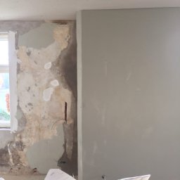 MADO Mateusz Dowejko - Ściana w trakcie szpachlowania: fragment surowej ściany obok gładkiej, wyszpachlowanej powierzchni. Widoczne narzędzia i worek z zaprawą. Ujęcie z bliska.