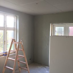 MADO Mateusz Dowejko - Pokój w trakcie szpachlowania: drewniana drabina przy oknie, ściany pokryte szpachlą, sufit z płyt karton-gips, wiadro z zaprawą na podłodze. Widoczne niedoskonałości.