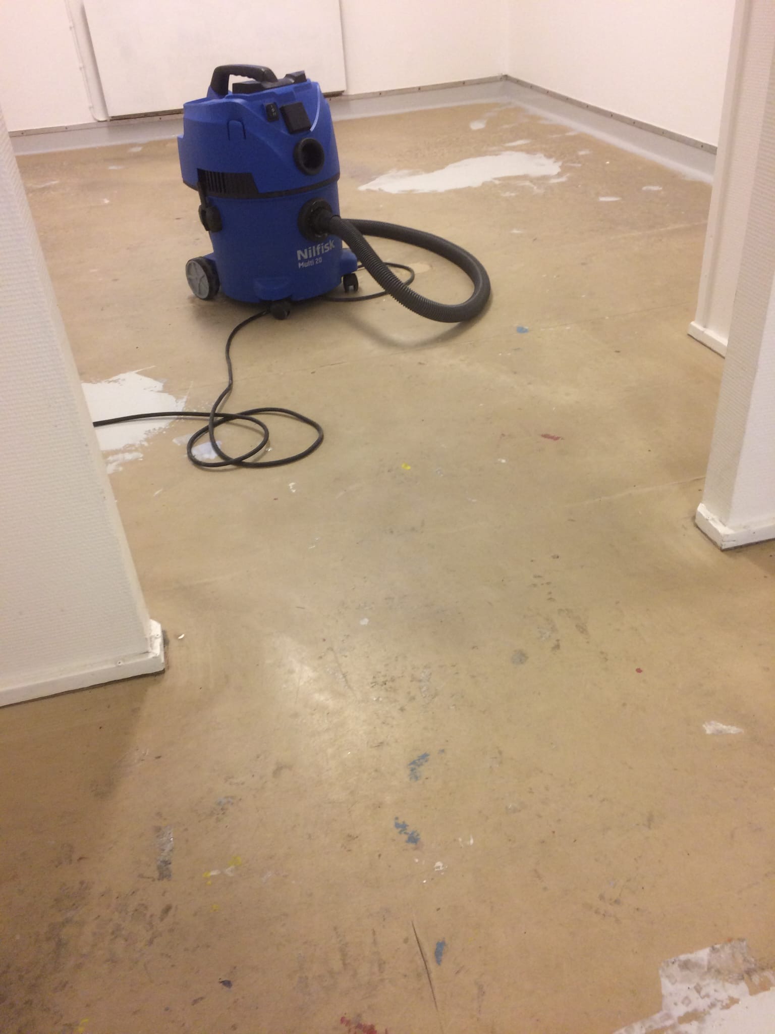 Przygotowanie podłoża pod posadzkę żywiczną: szlifowanie i odkurzanie. Widoczny odkurzacz przemysłowy Nilfisk Multi 20 i fragmenty starej posadzki.