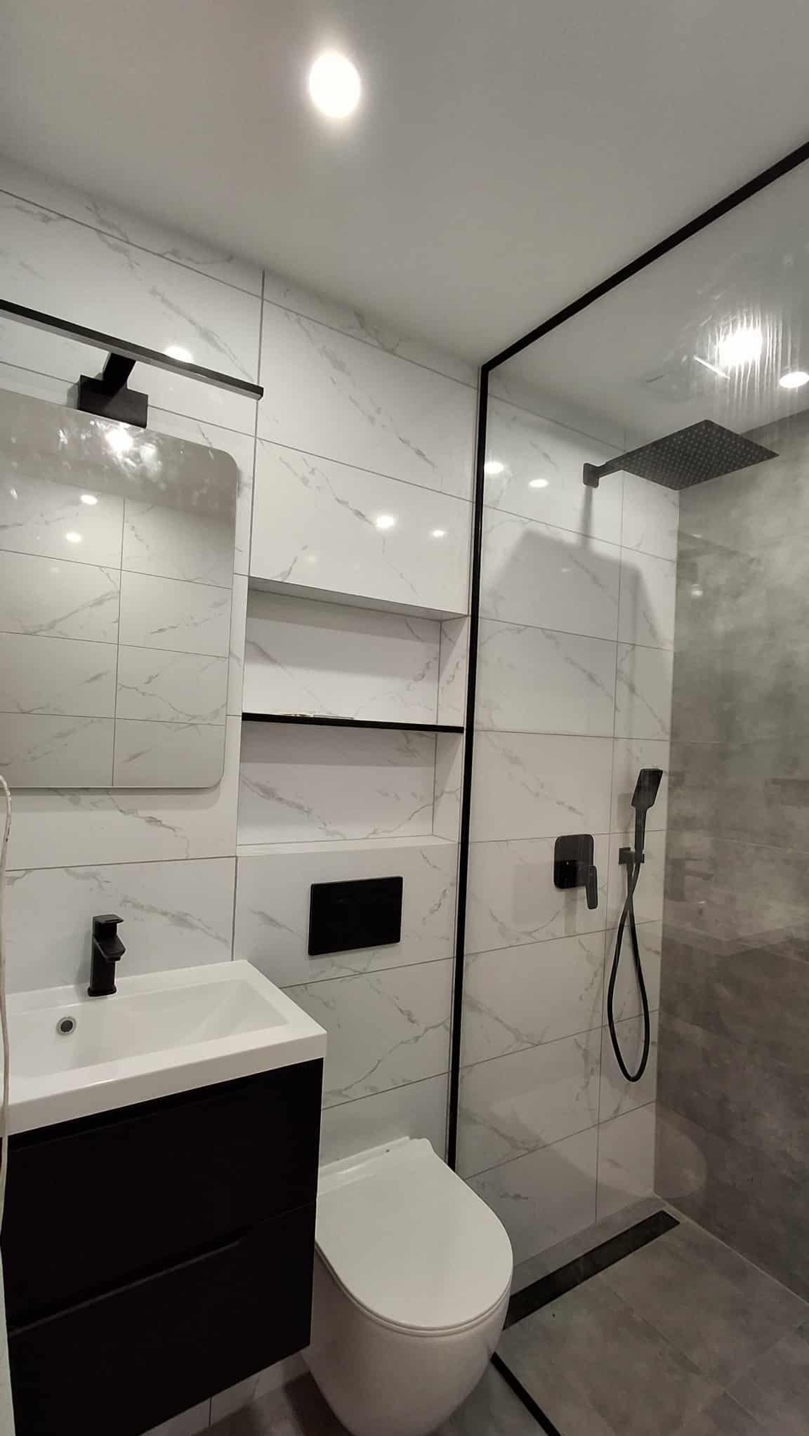 Nowoczesna łazienka w Turew z białymi płytkami imitującymi marmur, czarną armaturą i kabiną prysznicową typu walk-in. Minimalistyczny design i eleganckie wykończenie.