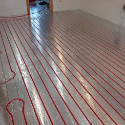 Envi-Technik Przemysław Ruszczyński - Czerwone rury ogrzewania podłogowego ułożone na srebrnej folii izolacyjnej, widok z góry na dużą powierzchnię w trakcie montażu.