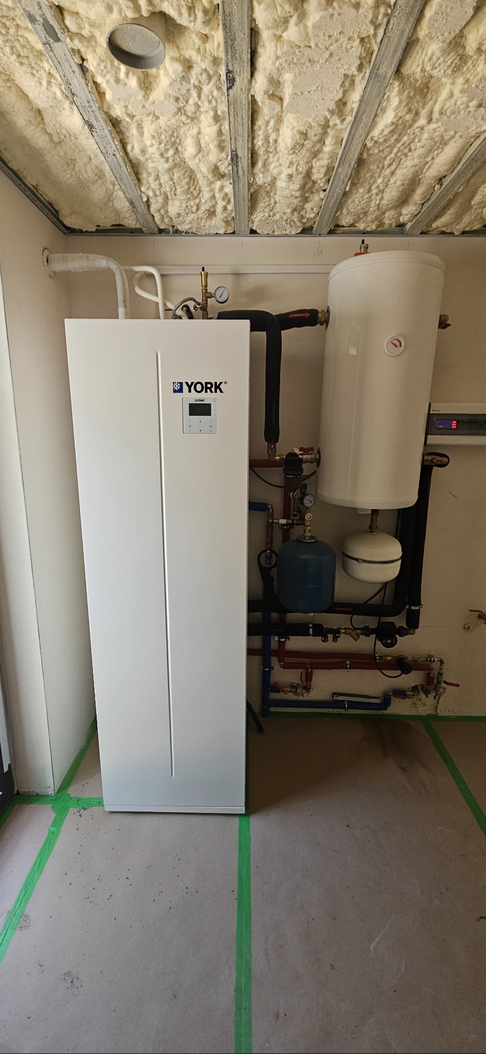 Biała pompa ciepła York z zbiornikiem, rurami i izolacją sufitu pianką PUR. Widoczne zielone linie wyznaczające obszar montażu.