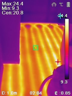 Obraz termowizyjny ogrzewania podłogowego w trakcie testów, gdzie temperatura jest oznaczona kolorami. Widoczne parametry pomiarowe na ekranie.