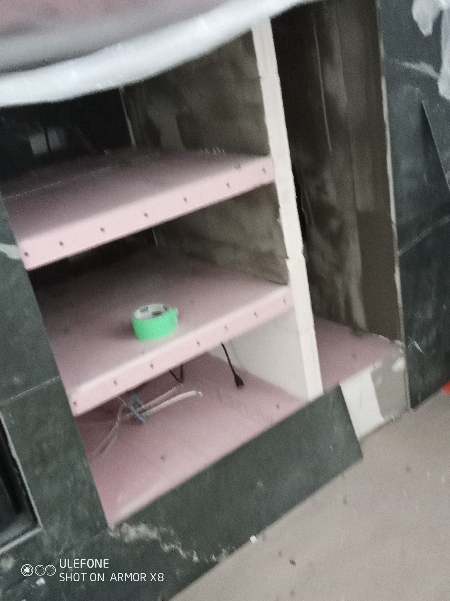 Narożna konstrukcja z płyt GK w trakcie zabudowy w łazience, widoczne kable i taśma malarska. Prace wykończeniowe, surowy stan.