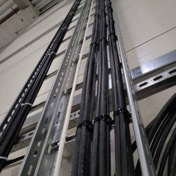 Parsbud Sp.z.o.oo - Ułożone kable w korytkach na ścianie, zabezpieczone opaskami. Widok z dołu ukazuje równoległe ułożenie przewodów i elementy mocujące do ściany.