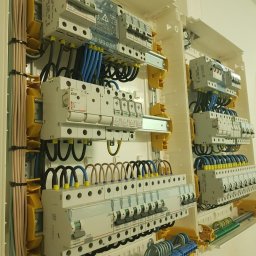 Parsbud Sp.z.o.oo - Rozdzielnica elektryczna z zainstalowanymi bezpiecznikami i okablowaniem w kolorach niebieskim, brązowym i czarnym. Widoczne elementy marki Legrand w jasnej obudowie.