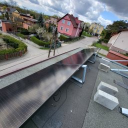 Parsbud Sp.z.o.oo - Montaż paneli fotowoltaicznych na dachu domu jednorodzinnego, widok z góry na częściowo zamontowaną instalację, w tle zabudowa mieszkalna i fragment nieba.