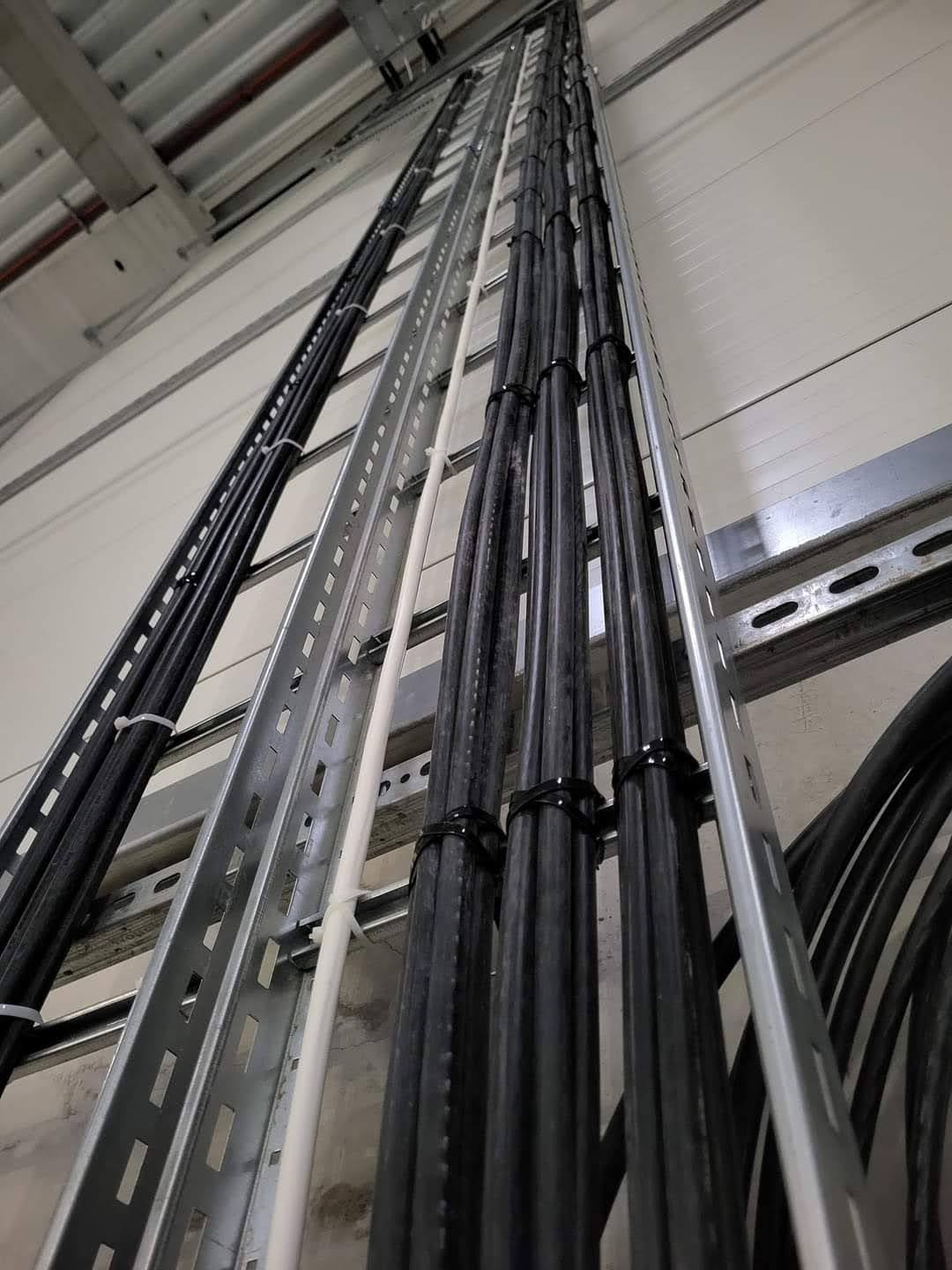 Ułożone kable w korytkach na ścianie, zabezpieczone opaskami. Widok z dołu ukazuje równoległe ułożenie przewodów i elementy mocujące do ściany.