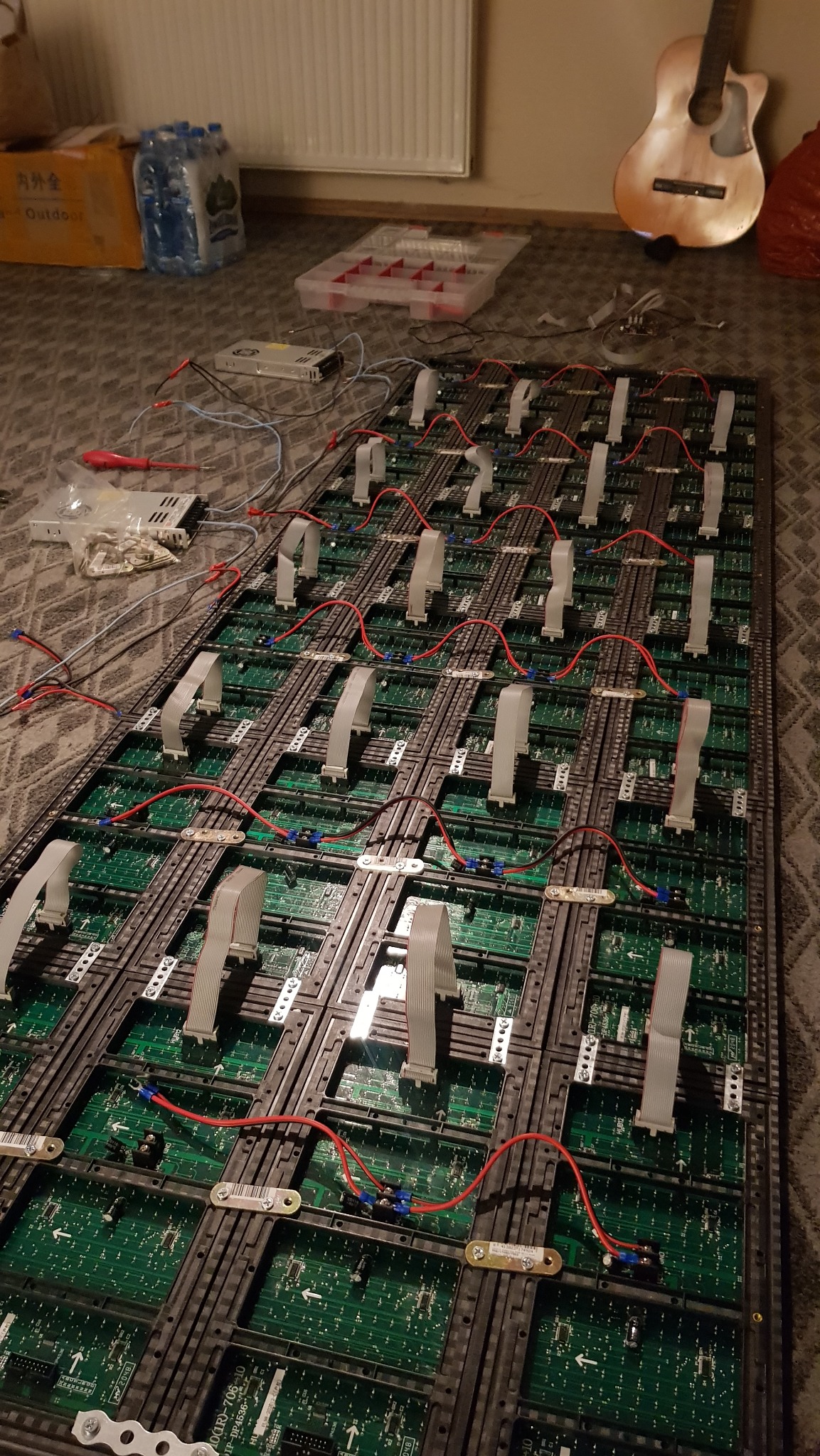 Panel LED w trakcie montażu: widoczne moduły, przewody i złącza. W tle narzędzia, zasilacz i gitara. Praca na podłodze z dywanem. Nietypowe hobby?