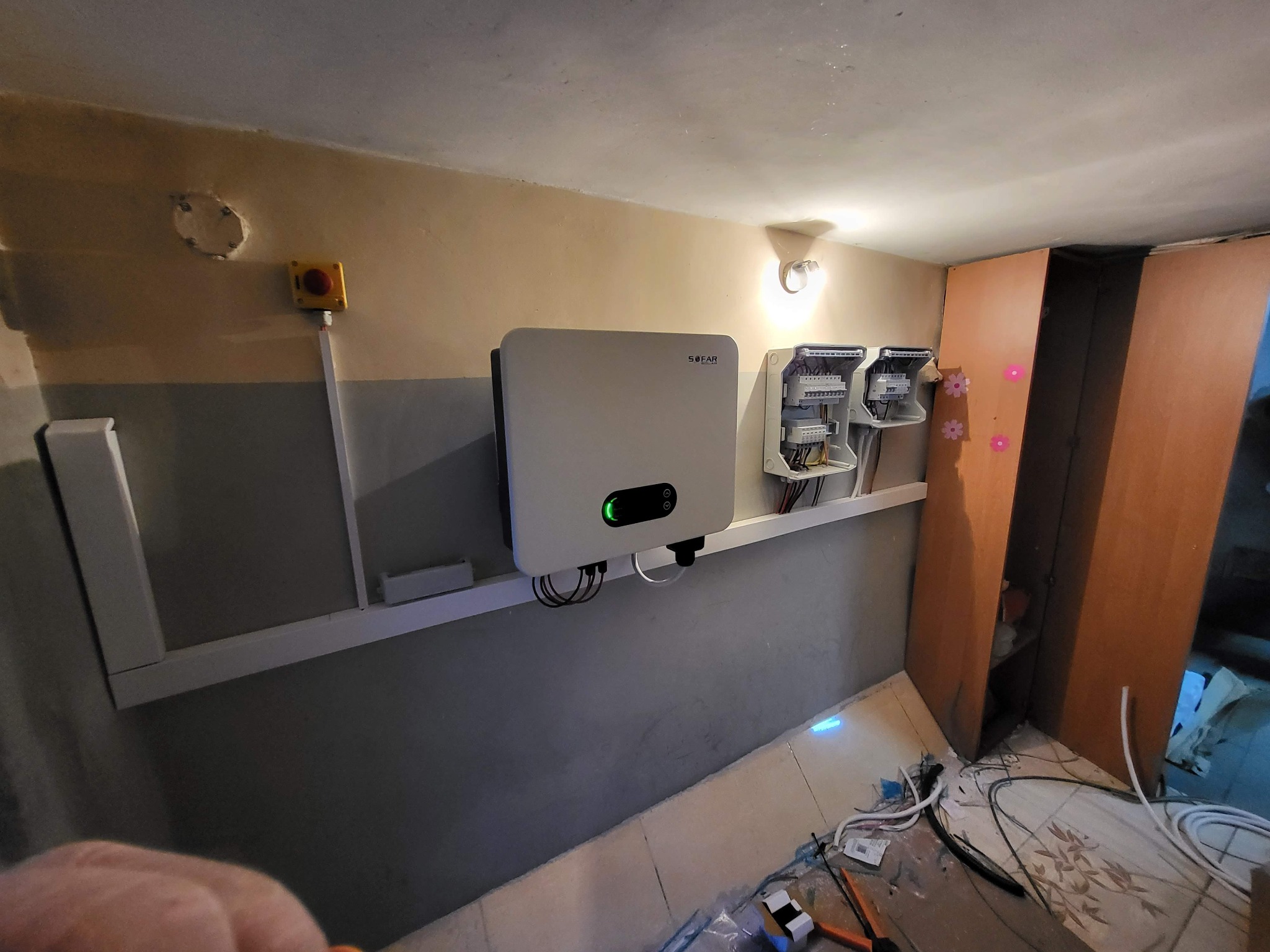 Zamontowany inwerter SOFAR z podłączonymi przewodami i rozdzielnicami na ścianie. Widoczne narzędzia na podłodze sugerują etap instalacji.