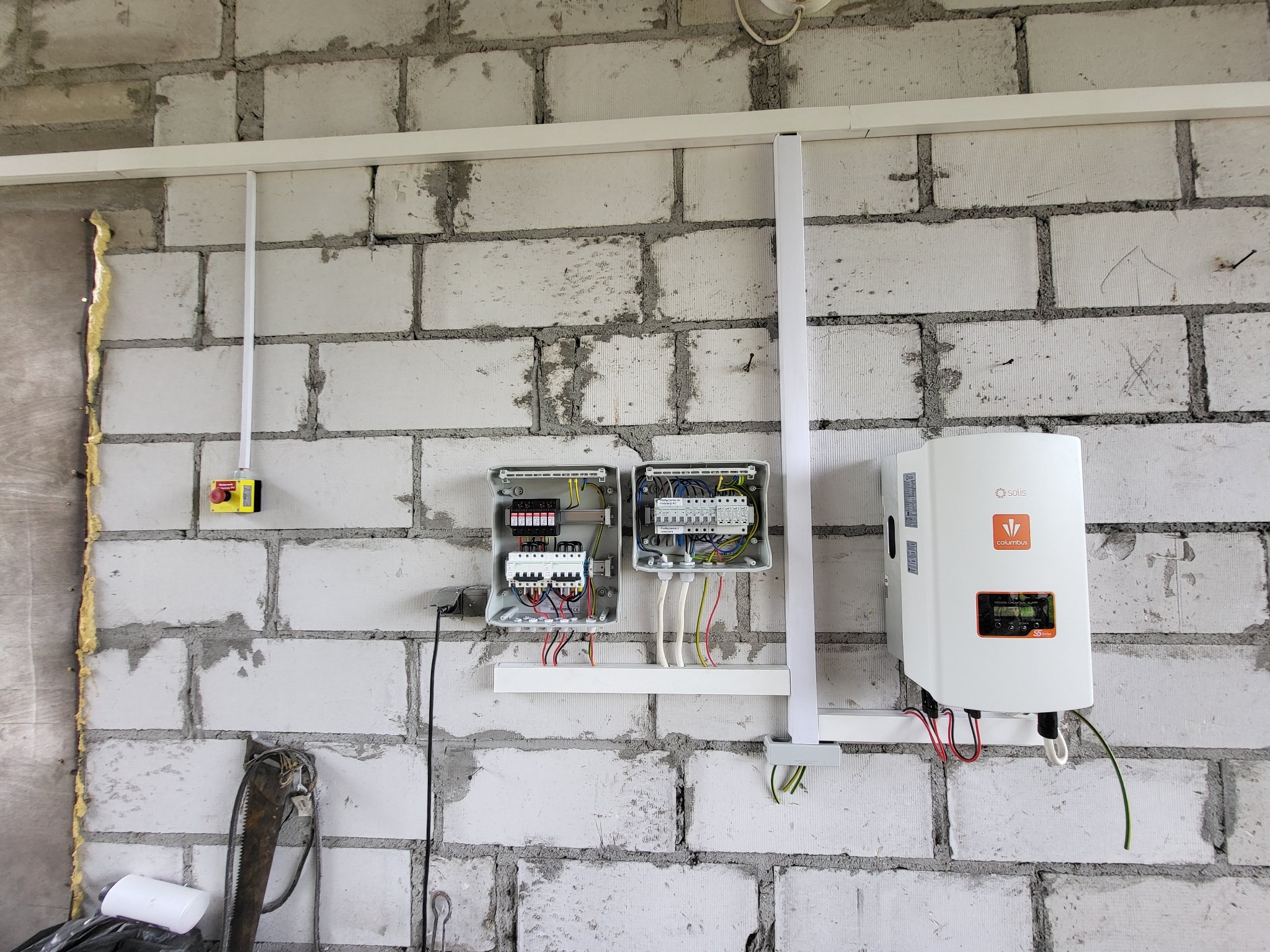 Dwa otwarte rozdzielnice i inwerter Columbus na ścianie z białego gazobetonu. Instalacja elektryczna wewnątrz budynku w trakcie montażu.