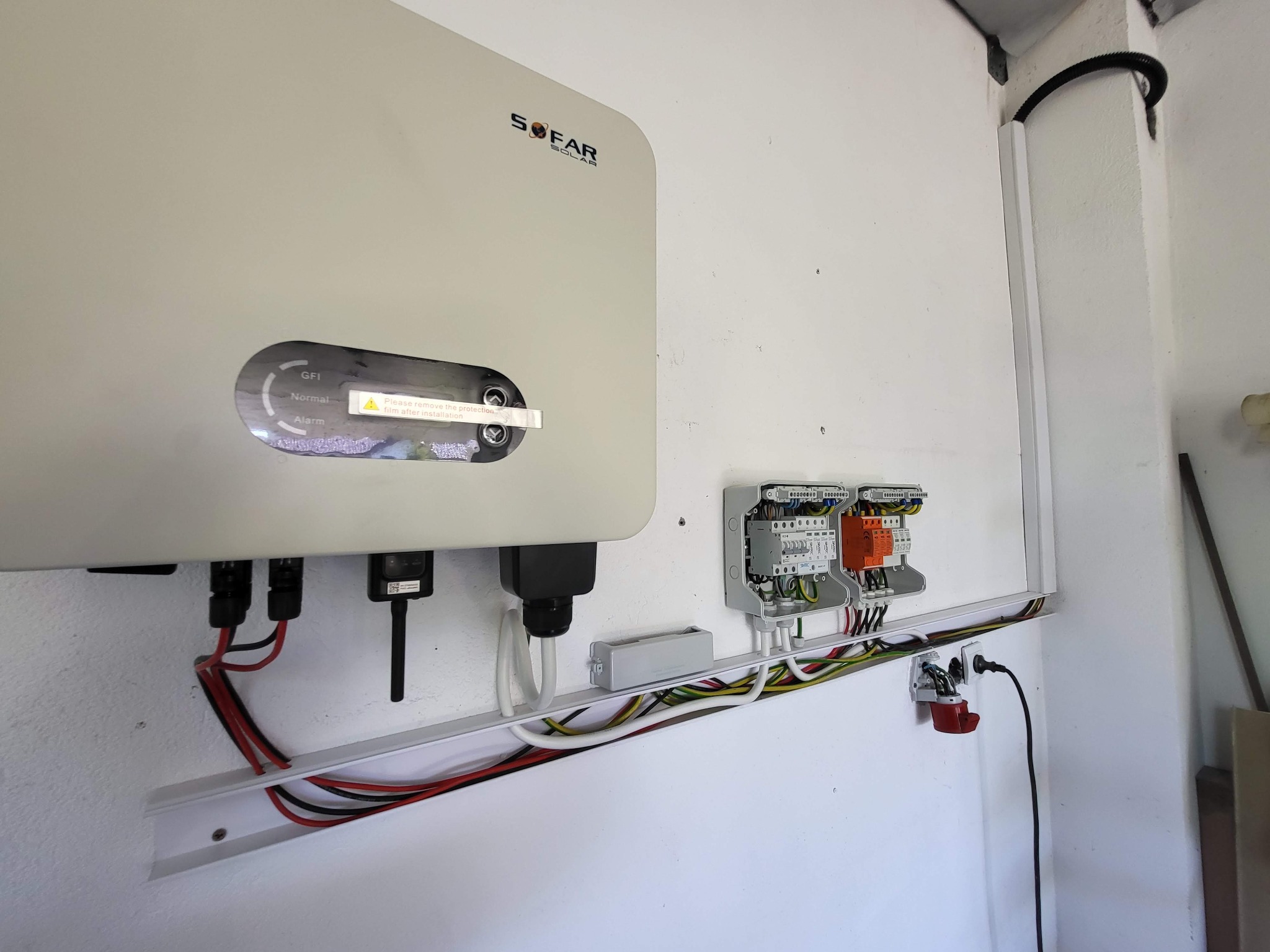 Biały falownik Sofar Solar zamontowany na ścianie, z widocznymi kablami i zabezpieczeniami w listwie. Widoczny wskaźnik GFI.
