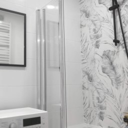 Oksana Yepik - Nowoczesna łazienka z wanną i czarną armaturą, kabina prysznicowa ze srebrnymi profilami, wzorzyste płytki na ścianie. Widoczna pralka i lustro.