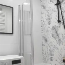 Nowoczesna łazienka z wanną i czarną armaturą, kabina prysznicowa ze srebrnymi profilami, wzorzyste płytki na ścianie. Widoczna pralka i lustro.