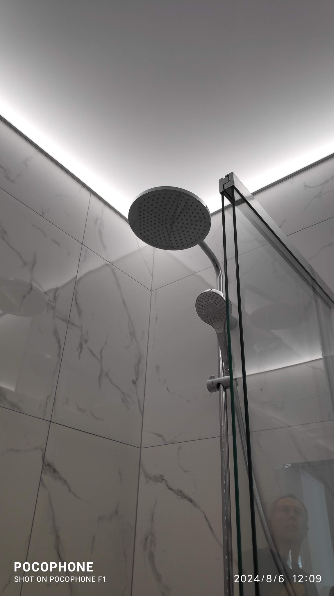 Nowoczesna kabina prysznicowa z deszczownicą i szklaną ścianką, wykończona płytkami imitującymi marmur, podświetlona listwą LED. Minimalistyczny design.