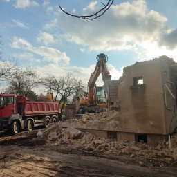 Tcf-Żwirownia - Ciężki sprzęt (koparka i wywrotka MAN) przy pozostałościach budynku w trakcie rozbiórki. Gruz i fragmenty ścian w otoczeniu. Błękitne niebo w tle.