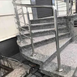 Zewnętrzne schody z szarego granitu z metalową balustradą, prowadzące do budynku. Widoczne detale wykończenia i faktura kamienia.