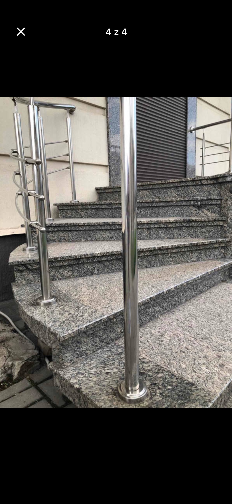 Spiralne schody zewnętrzne z szarego granitu z metalową balustradą, prowadzące do budynku z żaluzjami. Kąt ujęcia z dołu podkreśla zakrzywiony kształt.
