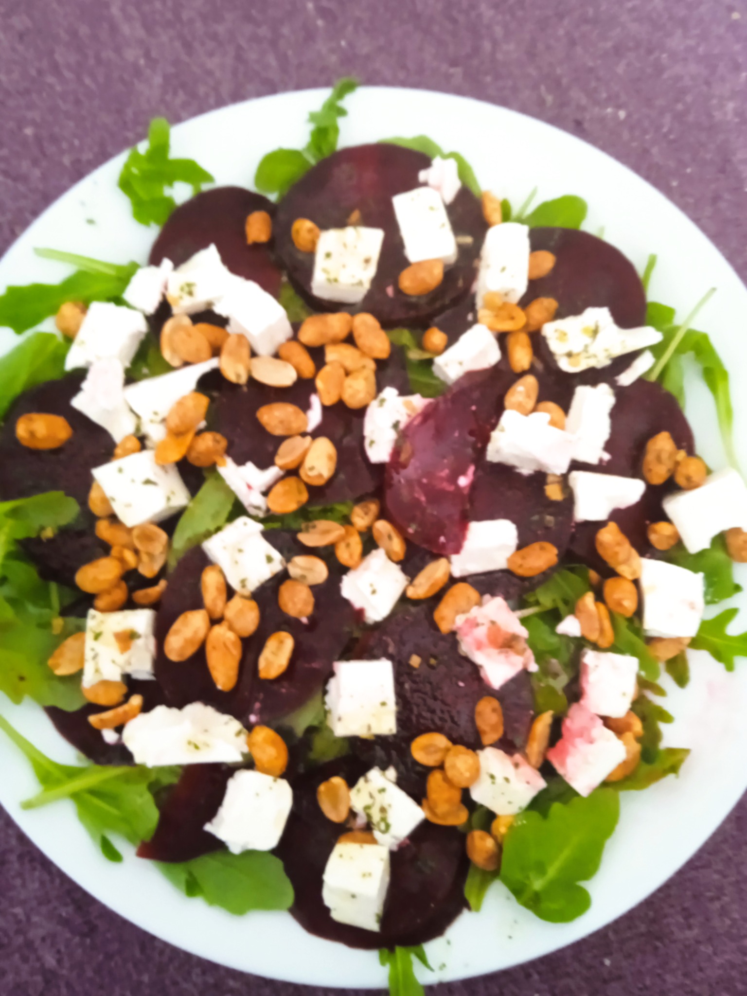 Sałatka z buraków, sera feta, orzechów i rukoli na białym talerzu, ułożona na fioletowym tle. Zdjęcie z góry, ukazujące świeżość i apetyczny wygląd dania.