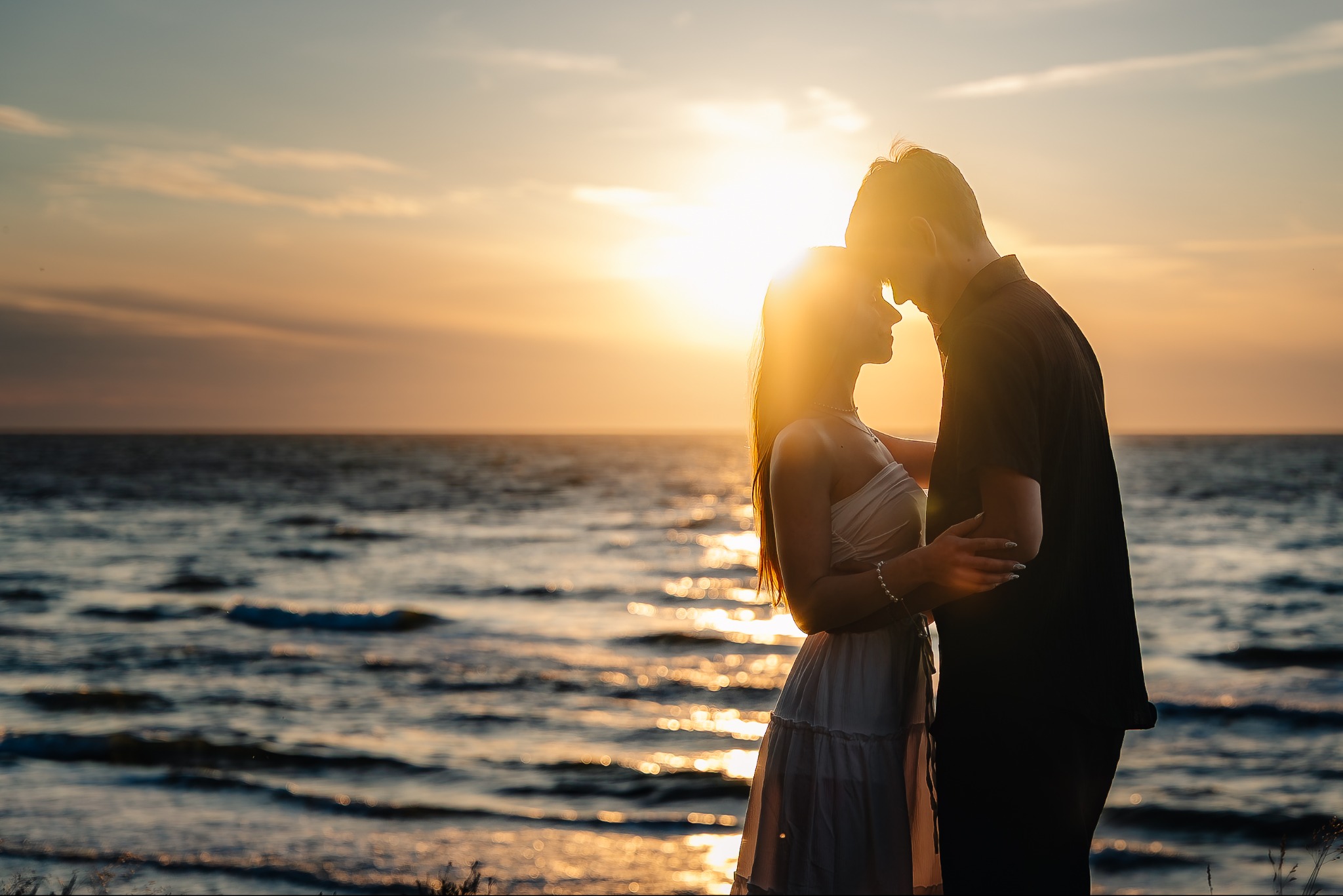 Zakochana para obejmuje się na tle morza i zachodzącego słońca. Silne, ciepłe światło słoneczne.