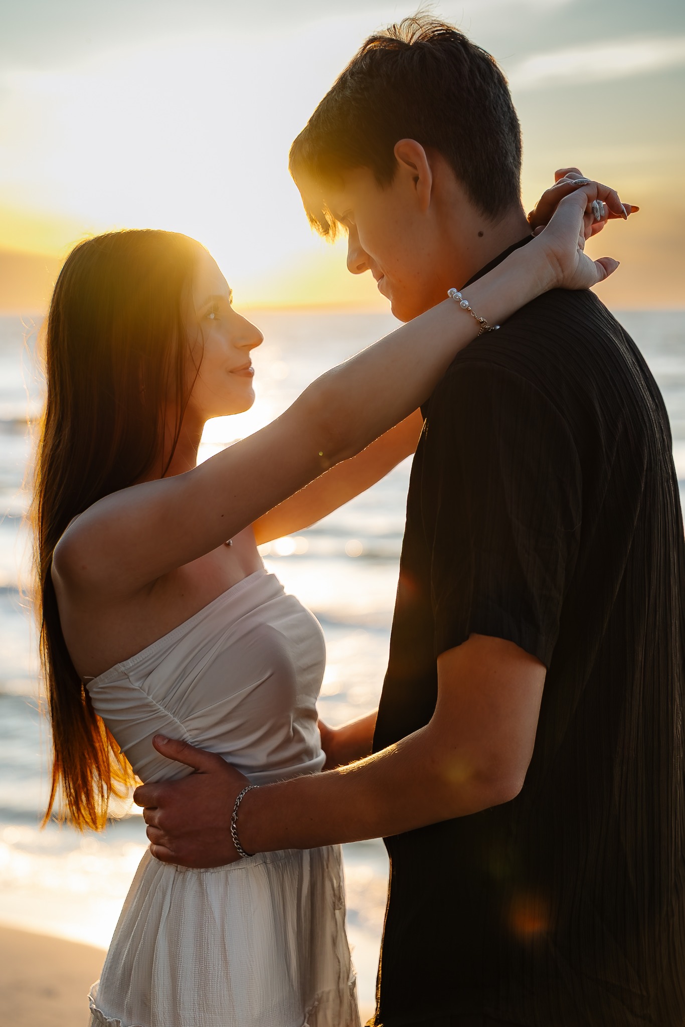 Zakochana para na plaży o zachodzie słońca. Kobieta obejmuje mężczyznę, oboje patrzą na siebie. Delikatne światło podkreśla romantyczny nastrój.