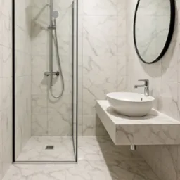 Nowoczesna łazienka z kabiną typu walk-in, białą umywalką na marmurowym blacie i okrągłym lustrem w czarnej ramie. Całość wykończona płytkami imitującymi marmur.