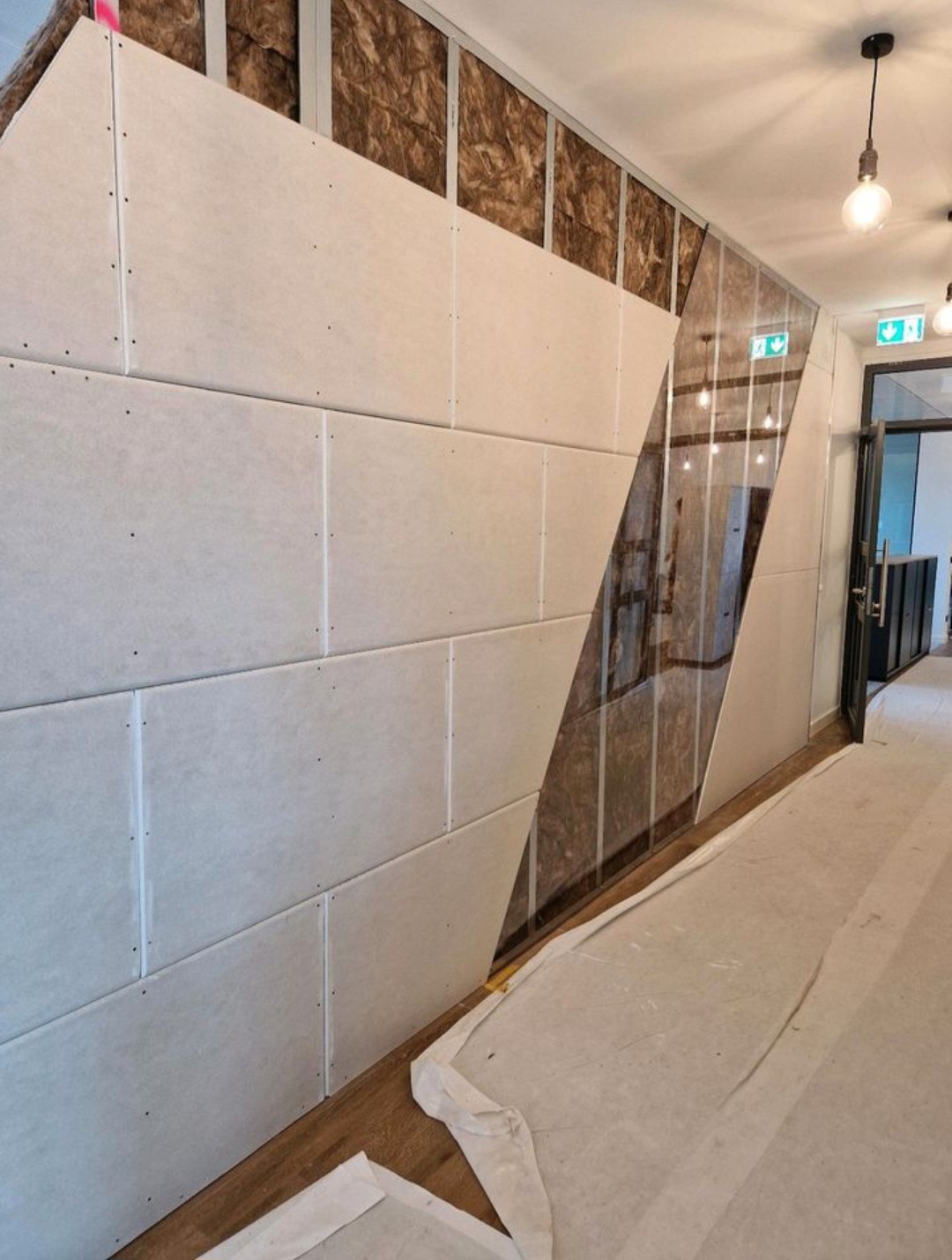 Wnętrze w trakcie wykańczania: widoczna izolacja ścian wełną mineralną i częściowo zamontowane płyty gipsowo-kartonowe. Podłoga zabezpieczona folią malarską.