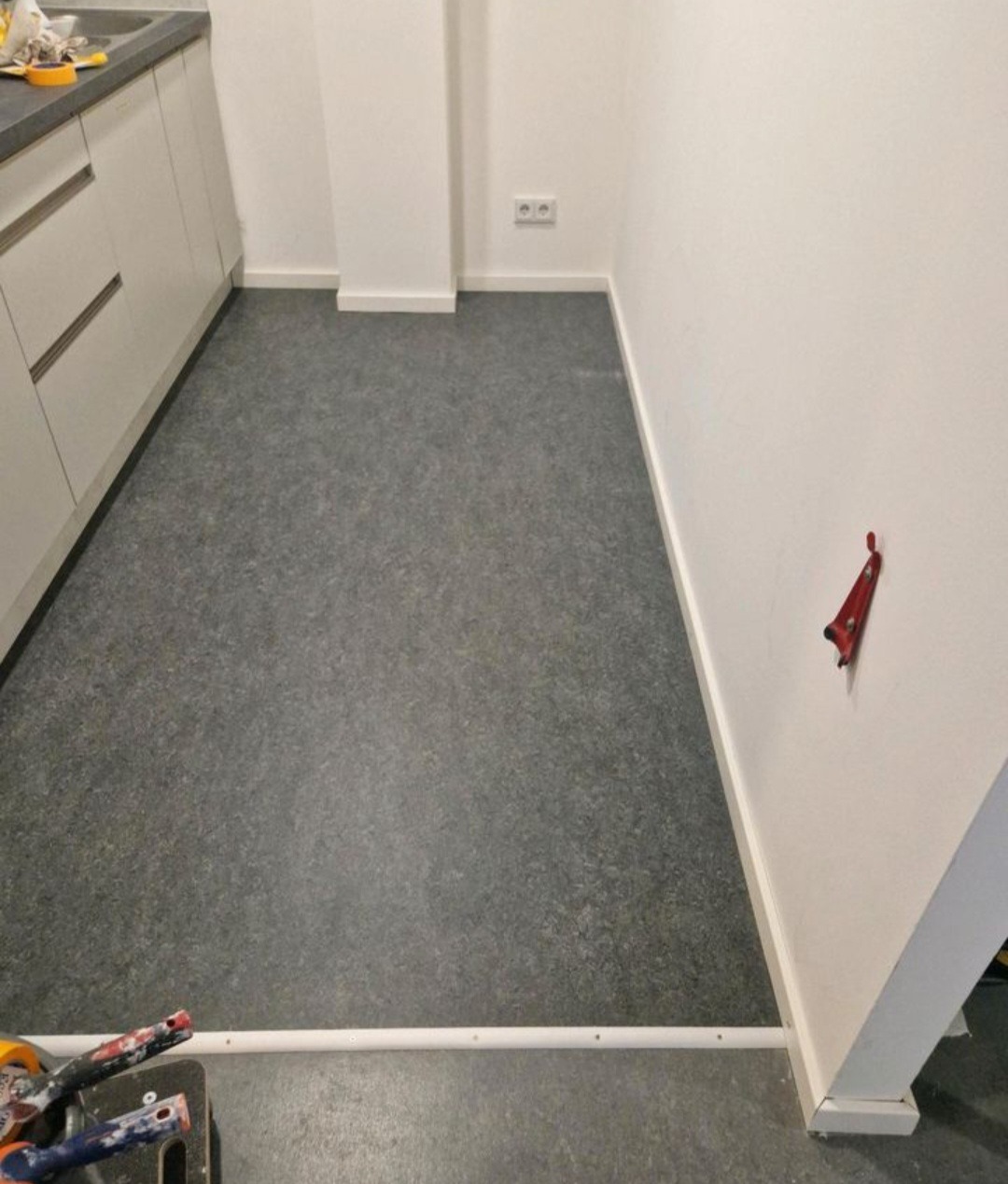 Ukończona podłoga z szarego linoleum w Dębicy, widok z góry. Częściowo widoczne białe szafki kuchenne i narzędzia glazurnicze w rogu.