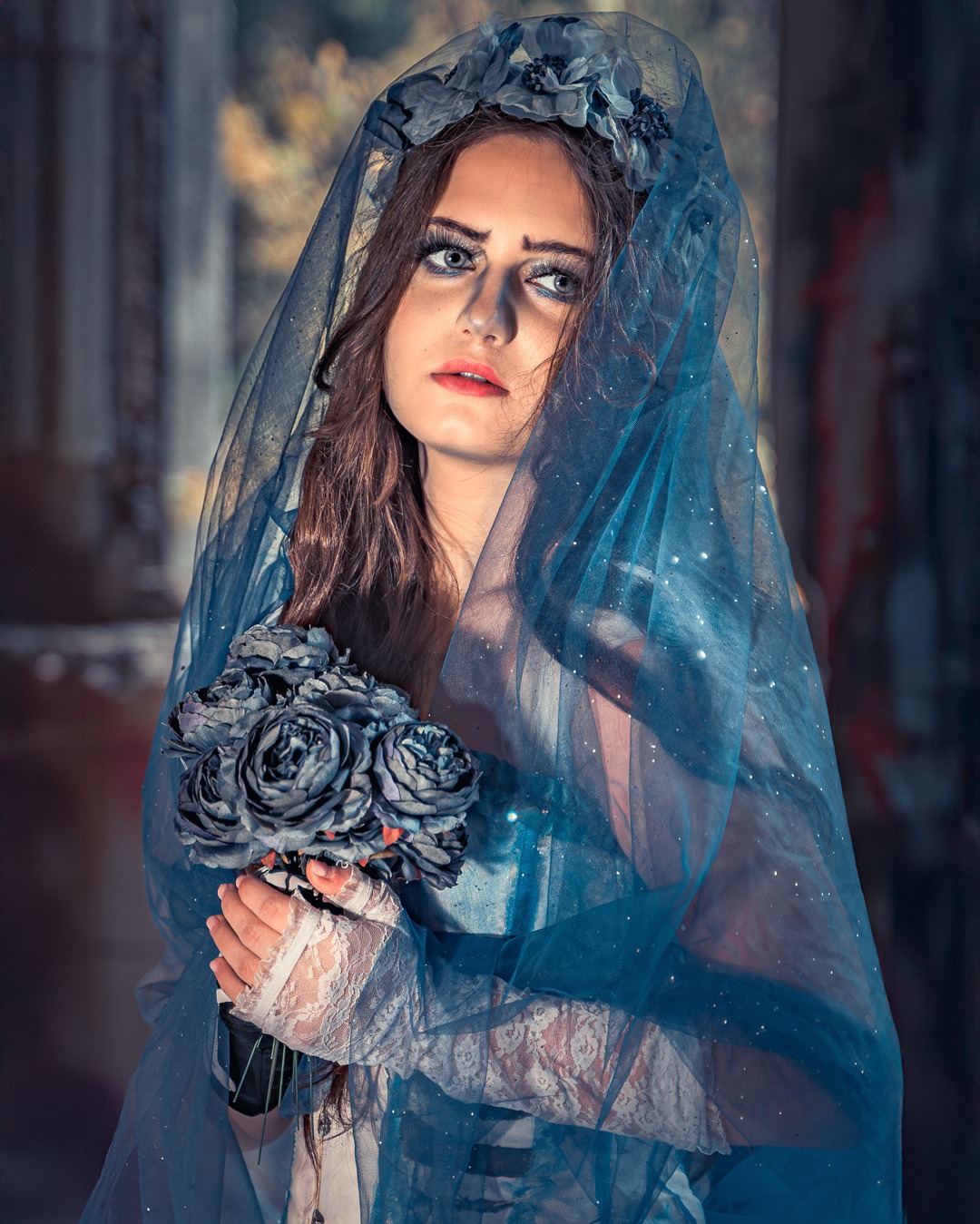 Portret kobiety w niebieskim welonie i z bukietem szarych róż, stylizowany na sesję kobiecą w mrocznym klimacie, z delikatnym oświetleniem i artystycznym tłem.