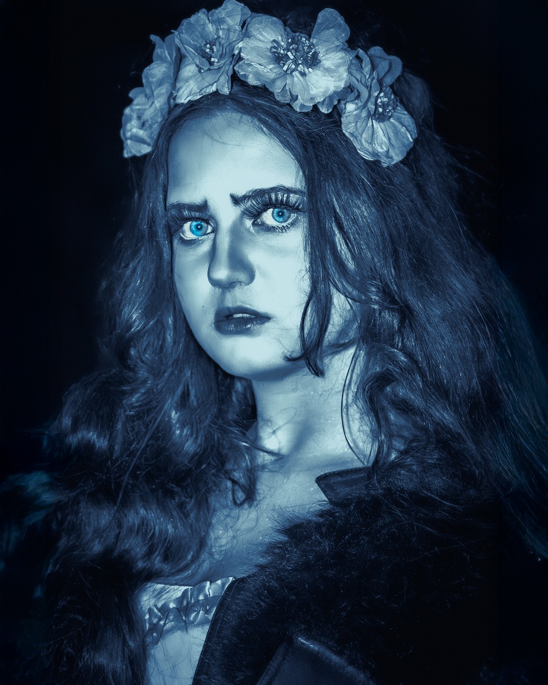 Portret kobiety z wiankiem na głowie, w chłodnej tonacji, z mocnym makijażem oczu i wyrazistym spojrzeniem, na ciemnym tle. Stylizacja inspirowana gotykiem.