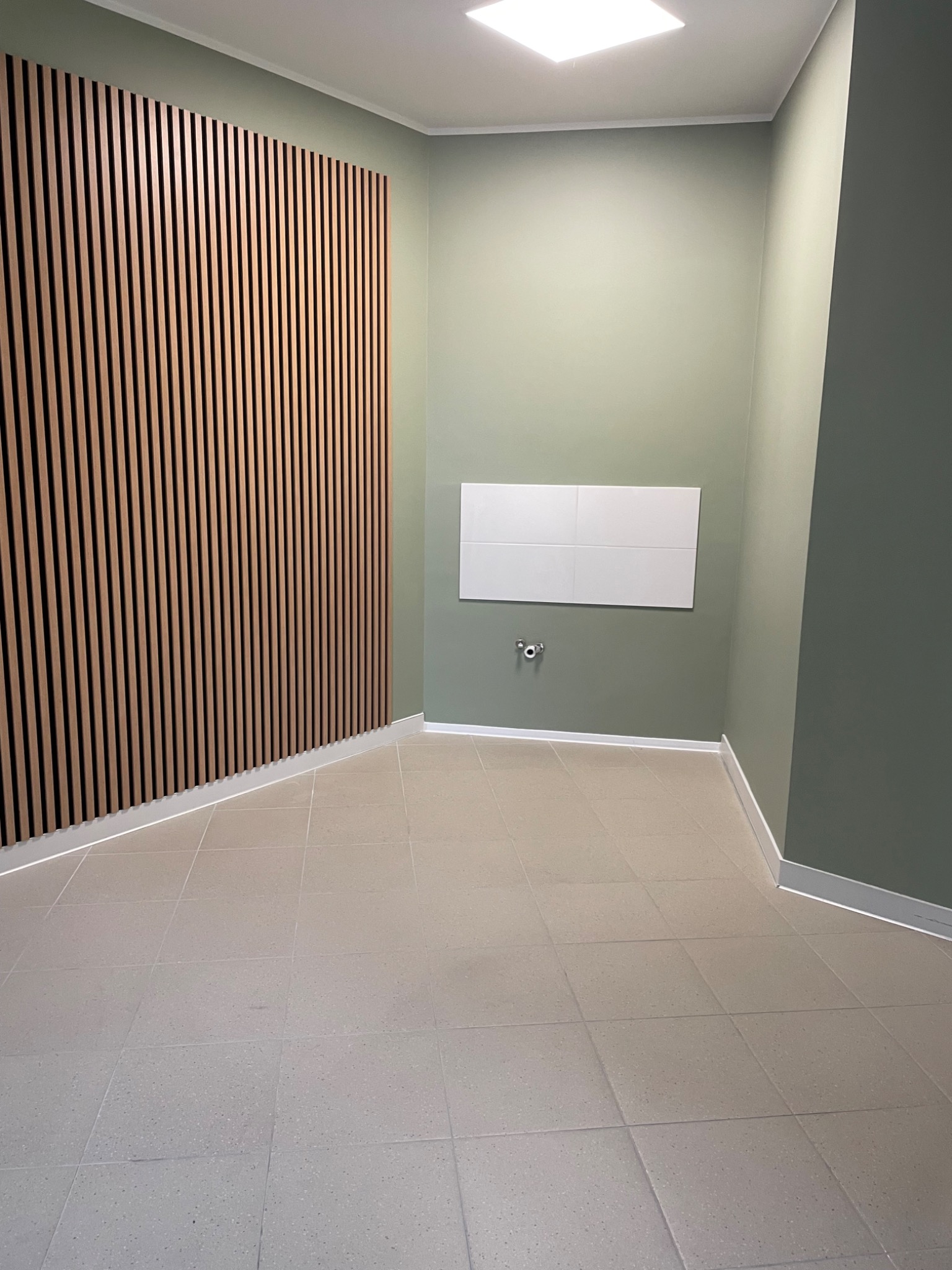 Wnętrze po remoncie: jasne płytki podłogowe, ściany w odcieniach zieleni, dekoracyjna drewniana listwa na ścianie. Minimalistyczny design, czystość i porządek.