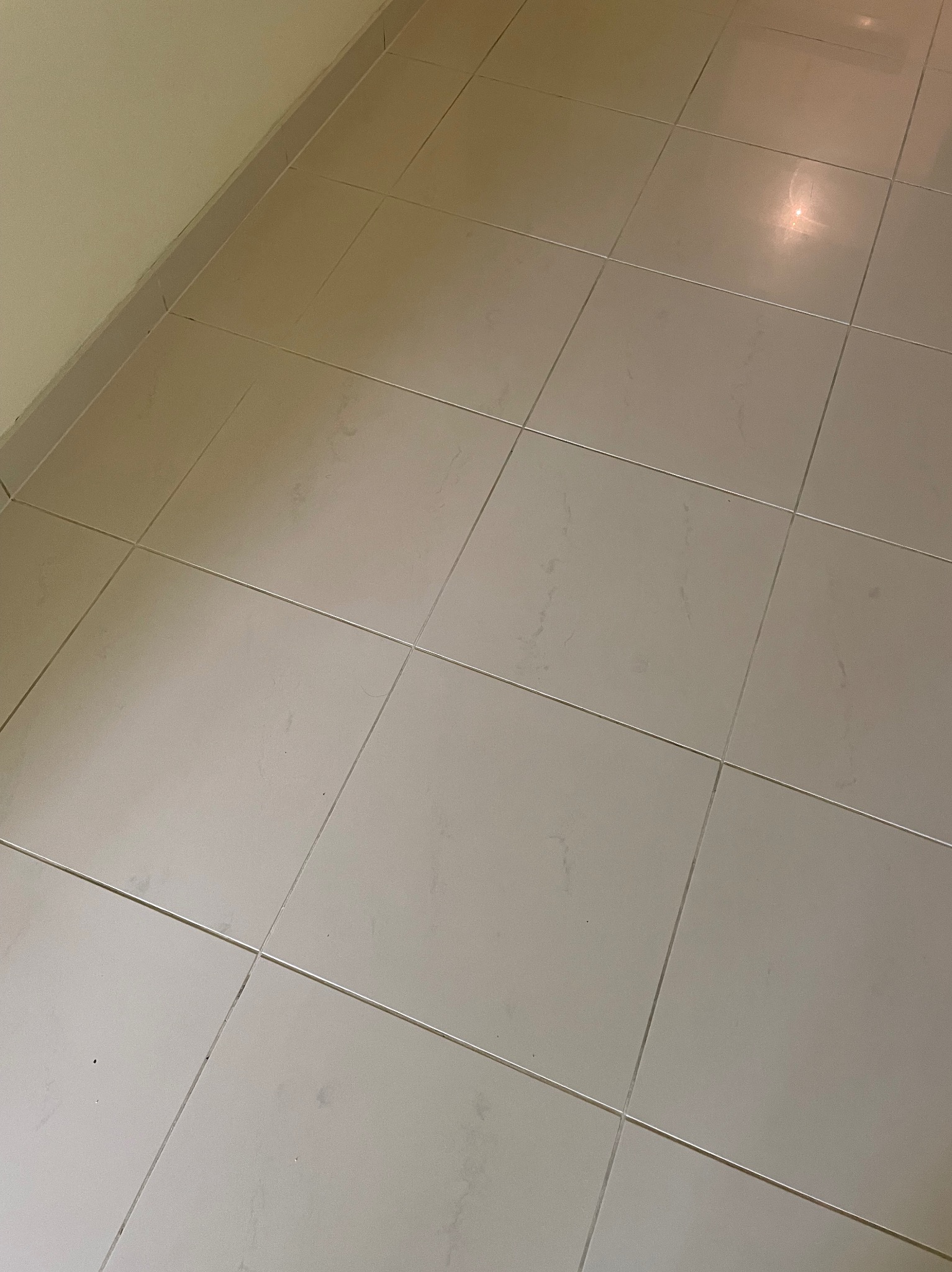 Jasne, umyte płytki podłogowe w pomieszczeniu, widoczne fugi i odbicie światła. Minimalistyczne ujęcie na czystą posadzkę po sprzątaniu.