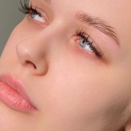 Makeup.Brows - Zbliżenie na twarz kobiety po zabiegu stylizacji brwi i rzęs. Widoczne gładkie, błyszczące brwi i wyraźnie podkreślone rzęsy. Delikatny makijaż.