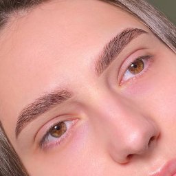 Makeup.Brows - Zbliżenie na brwi po zabiegu laminacji. Widoczne idealnie ułożone, ciemne włoski i naturalny efekt. Modelka ma jasną cerę i brązowe oczy.
