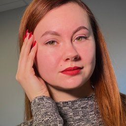 Makeup.Brows - Portret kobiety o rudych włosach z czerwonymi ustami i paznokciami, dłoń przy twarzy. Subtelny makijaż oczu i brwi. Szary sweter i jasne tło.
