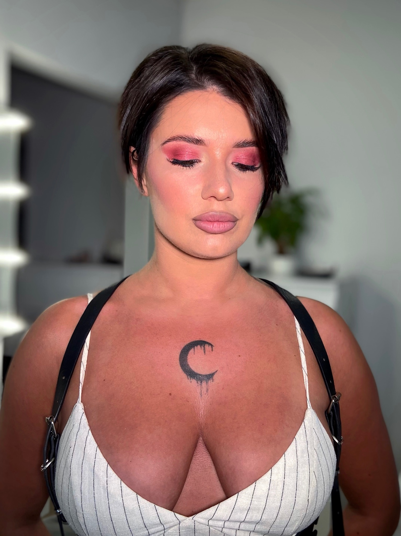 Kobieta z zamkniętymi oczami prezentuje różowy makijaż oczu i delikatny makijaż ust we Wrocławiu. Widoczny tatuaż na dekolcie i uprząż.