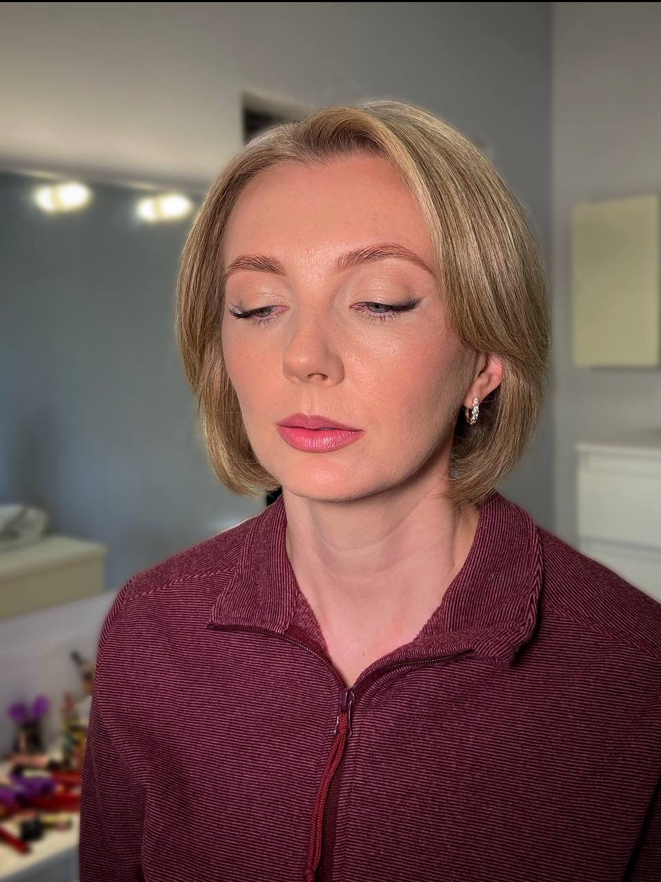 Delikatny makijaż dzienny z precyzyjną kreską na powiece i różowymi ustami, podkreślający urodę kobiety o krótkich blond włosach i subtelnej biżuterii.